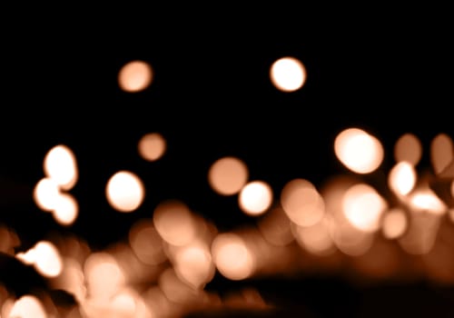 Blurry garland lights on a dark background. Festive Christmas and New Year background. Soft focus. Image toned in color of the year 2024 - Peach Fuzz.