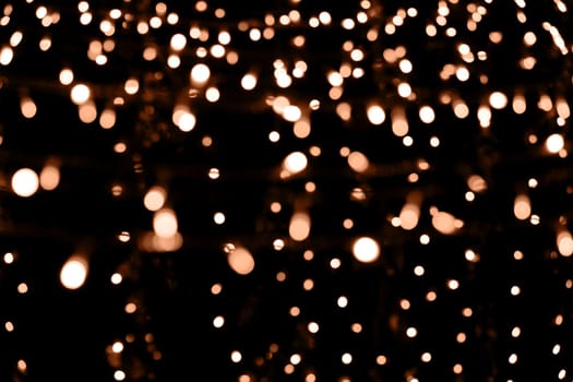 Blurry garland lights on a dark background. Festive Christmas and New Year background. Soft focus. Image toned in color of the year 2024 - Peach Fuzz.