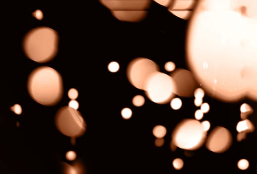 Blurry garland lights on a dark background. Festive Christmas and New Year background. Soft focus. Image toned in color of the year 2024 - Peach Fuzz.