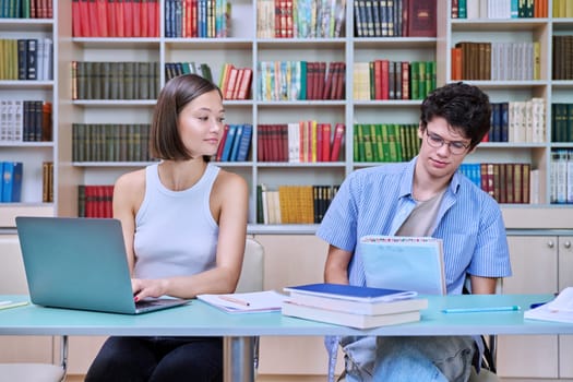 Young male and female students sitting at desk in college library, with books, notebooks, studying, preparing for exams. Knowledge, education, youth, college university concept