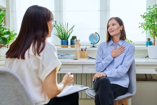 Young woman at a mental therapy session talking to female psychologist in therapist's office. Smiling female patient, help support professional counselor, psychotherapist, mental health youth concept