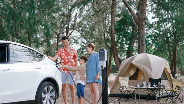 Outdoor adventure and family vacation camping in nature travel by eco friendly car for sustainable future. Lovely family recharge EV car with EV charging station in campsite. Perpetual