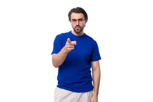 A 30 year old surprised European guy with black hair and a beard in a blue T-shirt points to the space for advertising.