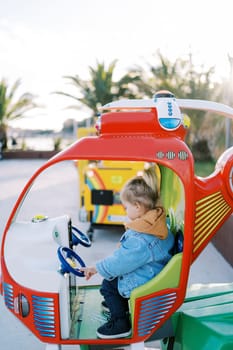 Little girl sits in the cockpit of a toy helicopter and touches the steering wheel on the playground. High quality photo