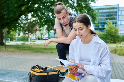 Two high school students guy and girl outdoor, school building background. Education, friendship, youth, adolescence concept