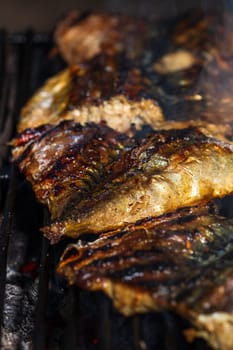 Grilled mackerel fish with smoke on a charcoal barbecue grill.