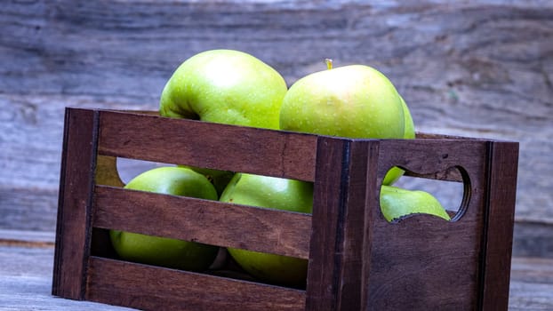 Wooden crate with ripe green apples on wooden table.