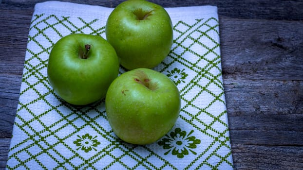 Ripe green apples on a rustic napkin on wooden table.