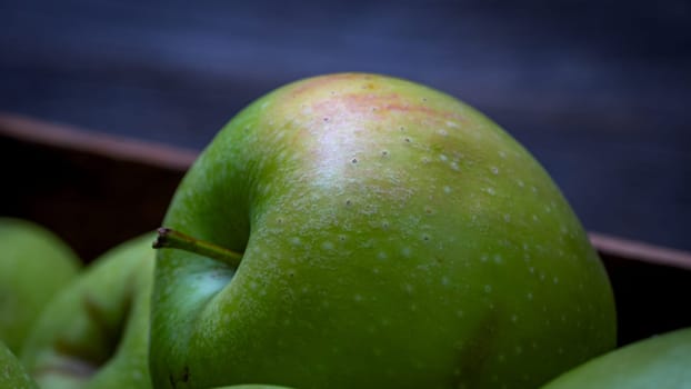 Wooden crate with ripe green apples on wooden table.