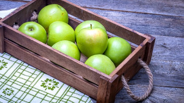 Wooden crate with ripe green apples on wooden table.