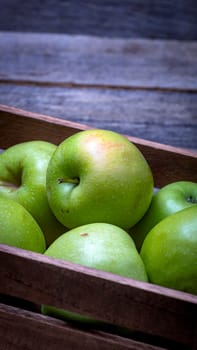 Wooden crate with ripe green apples on wooden table.