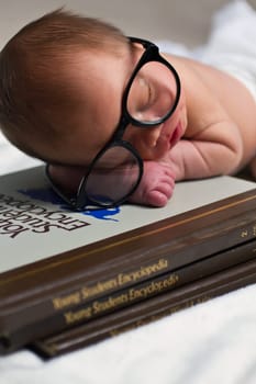 Whimsical Baby Scholar: A newborn lies atop a stack of books, donning oversized glasses, as if lost in a world of knowledge. This endearing image captures the early thirst for learning and the potential of youth.