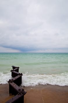 Tranquil beach scene on Lake Michigan with weathered metal structures reaching into the water. Moody sky adds to the serene atmosphere. Perfect for themes of nature, tranquility, and the passage of time.
