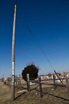 Rustic religious inspiration: A weathered wooden utility pole adorned with signs spelling out 'JESUS HOPE' stands against a clear blue sky. In the background, a peaceful cemetery with scattered gravestones.