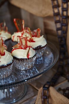 Decadent gourmet cupcakes with rich chocolate bases and a swirl of creamy white frosting, adorned with red stained glass candy and a drizzle of fruity syrup. Perfect for promoting luxury desserts and high-end bakeries. Culinary, Dessert, Food.