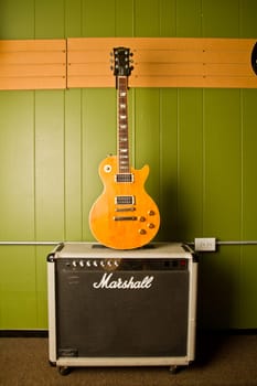 Rock and Roll Vibes: A sunburst electric guitar leans against a green wall, contrasting sharply and drawing attention to its sleek, polished body. The iconic Marshall amplifier stands ready for performance, evoking power and presence.