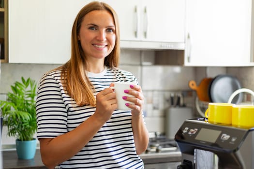 Young woman enjoying freshly prepared aromatic coffee near modern coffee machine in kitchen.
