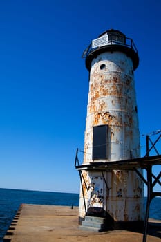 Enduring the test of time, an old lighthouse stands tall and rusted against a vivid blue sky, a beacon of maritime history on a concrete pier along the Michigan coast.