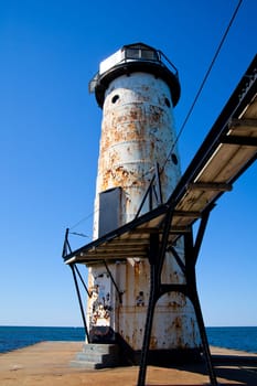 Timeless maritime charm: A weathered Michigan lighthouse stands tall against the blue sky, revealing its resilience to the harsh marine conditions. Rust and peeling paint add character, while a sailboat in the distance evokes tranquility.