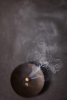 Abstract shot of a recently incense burning from above, releasing delicate wisps of smoke against a blurred background. Captures the ephemeral nature of moments and sparks of creativity. Tranquil and minimalist.