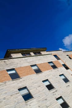 Modern architectural masterpiece in Bloomington, Indiana, showcasing a textured stone fasade with alternating materials and striking orange brickwork accent. Reflective windows and expansive blue sky evoke a sense of aspiration and progress.