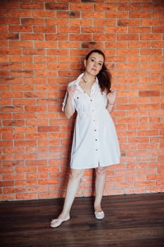 brunette woman in dress standing against brick wall