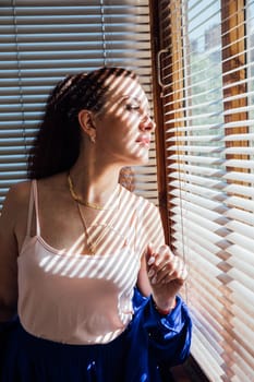 brunette woman light and shadow blinds from window