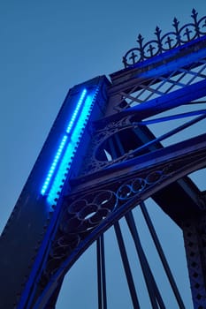 Captivating twilight view of the ornate metalwork and vibrant blue LED lights on the Wells Street Bridge in downtown Fort Wayne, Indiana. A perfect blend of historical architecture and modern lighting, showcasing the grandeur of urban infrastructure.