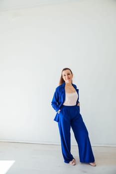 Beautiful brunette woman in blue summer suit posing in white room