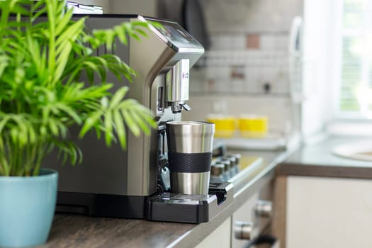 Modern electric coffee machine with cup on countertop in kitchen.