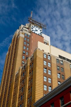 Vintage Clock Tower in Lansing: Capturing the passage of time, this urban setting showcases a grand multistory building with a broken clock face against a clear blue sky. Its orange and brown fasade and uniform windows evoke