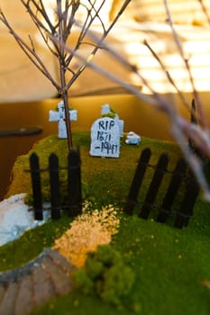 Meticulously crafted miniature graveyard scene with a focus on a headstone inscribed with 'RIP.' Surrounded by a black picket fence, the scene exudes a somber yet peaceful atmosphere.
