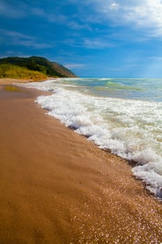 Experience the refreshing allure of a stunning beachscape on Lake Michigan. Feel the energy of crashing waves, golden sands, and lush green hills in this idyllic coastal getaway.