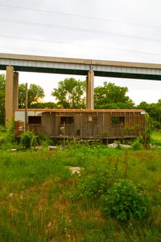 Desolate Urban Decay: Abandoned building overgrown with foliage in East St. Louis, Illinois, stands in stark contrast to a towering concrete bridge. Symbolizing the passage of time and the clash between nature and infrastructure.