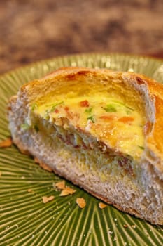 Savor the flavors of a golden-brown quiche in a bread bowl, featuring a vibrant yellow filling dotted with green herbs and pinkish-red pieces of ham or bacon. This homemade comfort food, captured in Fort Wayne, promises a gourmet brunch experience.