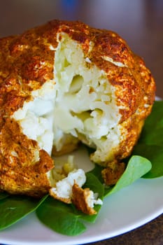 Roasted seasoned cauliflower on a bed of fresh spinach leaves, showcasing its golden-brown spiced crust. A mouthwatering vegetarian dish.