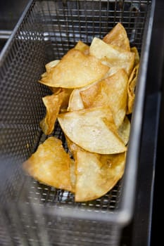 Golden-Brown Tortilla Chips Freshly Fried and Crispy in Metal Frying Basket. Perfectly Cooked Mexican Snack with Irregular Triangular Shapes.