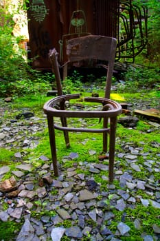 Nature's Resurgence: A weathered chair stands amidst urban decay, symbolizing neglect and desolation. Vibrant green moss engulfs broken tiles and debris, while a graffiti-tagged train car adds to the forgotten.