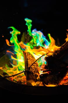 Experience the mesmerizing dance of vibrant flames in a captivating fire pit. The enchanting blend of green, blue, and traditional orange hues creates a magical display. Shot in a close-up perspective.