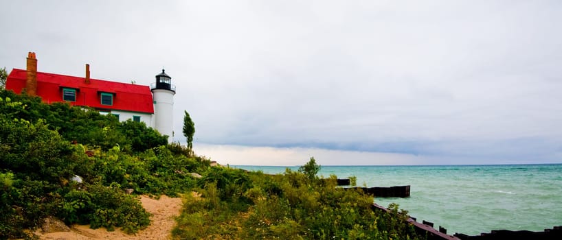 Serene coastal scene featuring a traditional lighthouse and its accompanying building nestled among lush greenery. Moody ambiance creates a sense of solitude and guidance by the turquoise waters of Lake Michigan.