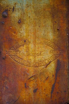 Vintage emblem of enduring quality amidst industrial decay in East of St. Louis Plant, Illinois. A rusted metal surface showcases a worn logo, symbolizing heritage and the passage of time.