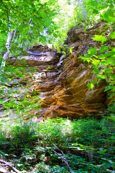 Nature's Majesty: A stunning rock formation amidst a lush forest in Fitzgerald County Park, Lansing, Michigan. The stratified sedimentary rocks in warm tones contrast with vibrant foliage, as sunlight filters through the canopy.
