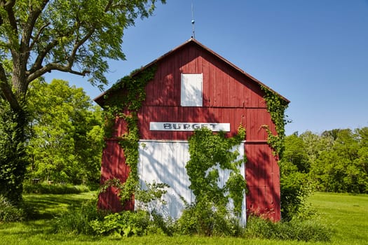 Rustic red barn with 'BURGET' sign surrounded by lush greenery in Fort Wayne, Indiana - a charming glimpse into rural heritage.