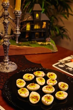 Spooky Halloween celebration with creatively garnished deviled eggs, atmospheric candelabra, and a miniature haunted house model.