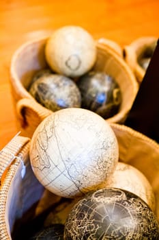 Vintage-style globes in sepia, black, and white tones are showcased in a woven basket, with a cream-colored globe featuring detailed Earth's surface. Perfect for travel, education, and interior design themes.
