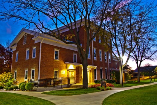 Serene twilight at a classic brick community center in Fort Wayne, Indiana. Warm lighting illuminates the traditional architecture. Perfect for marketing local services and highlighting community spirit.