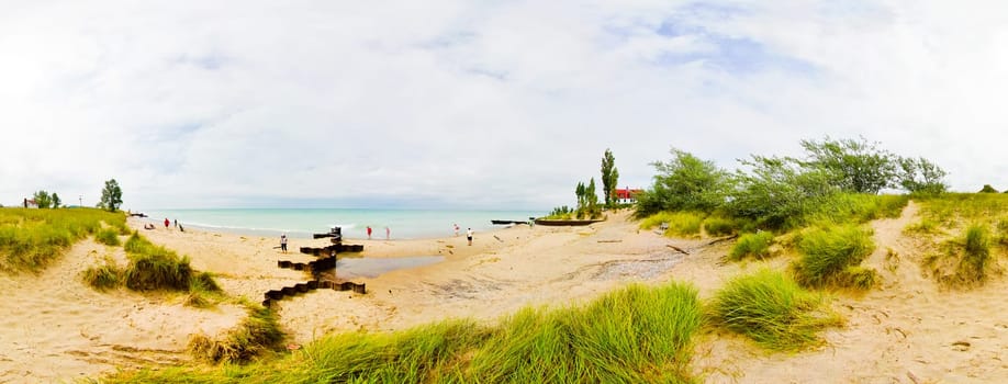 Tranquil sandy beach scene with expansive coastline, lush dune grasses, and a striking red-roofed building overlooking the calm turquoise waters. Perfect for travel, nature, and relaxation themes.