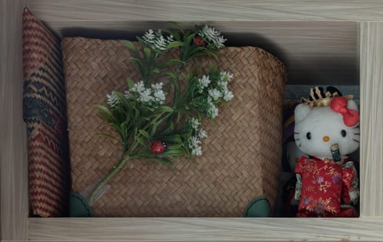 Bangkok, Thailand - jul 28, 2022 - Handmade Seagrass Basket with artificial flowers and Kimono doll "Hello Kitty" on wooden shelf. Space for text, Selective focus.