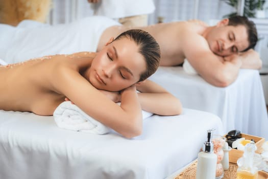 Blissful couple customer having exfoliation treatment in luxury spa salon with warmth candle light ambient. Salt scrub beauty treatment in health spa body scrub. Quiescent