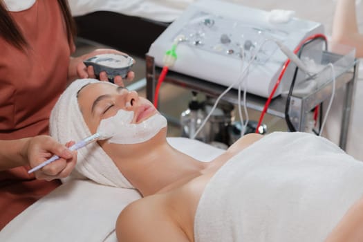 Beautiful young women lie on spa bed while having facial massage from professional doctor. Attractive female with beautiful skin surrounded by electric facial machine. Tranquility.